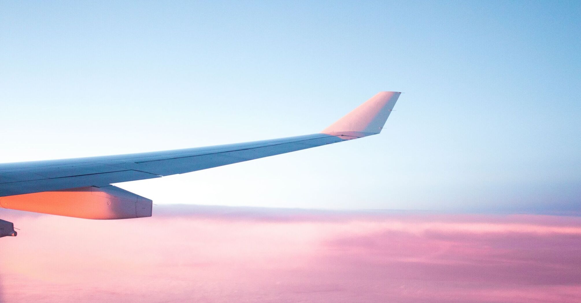 View of an airplane wing against a pastel pink sky during sunrise or sunset