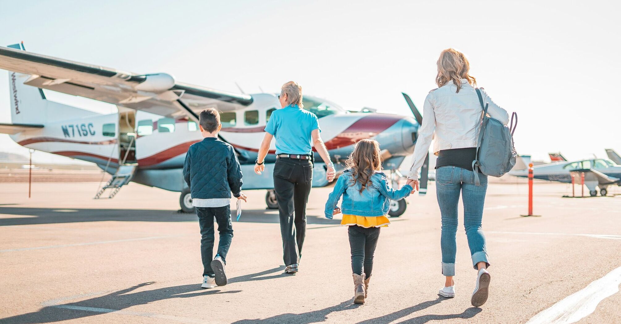 A family walking towards a small airplane on a tarmac, indicative of relaxed family travel 