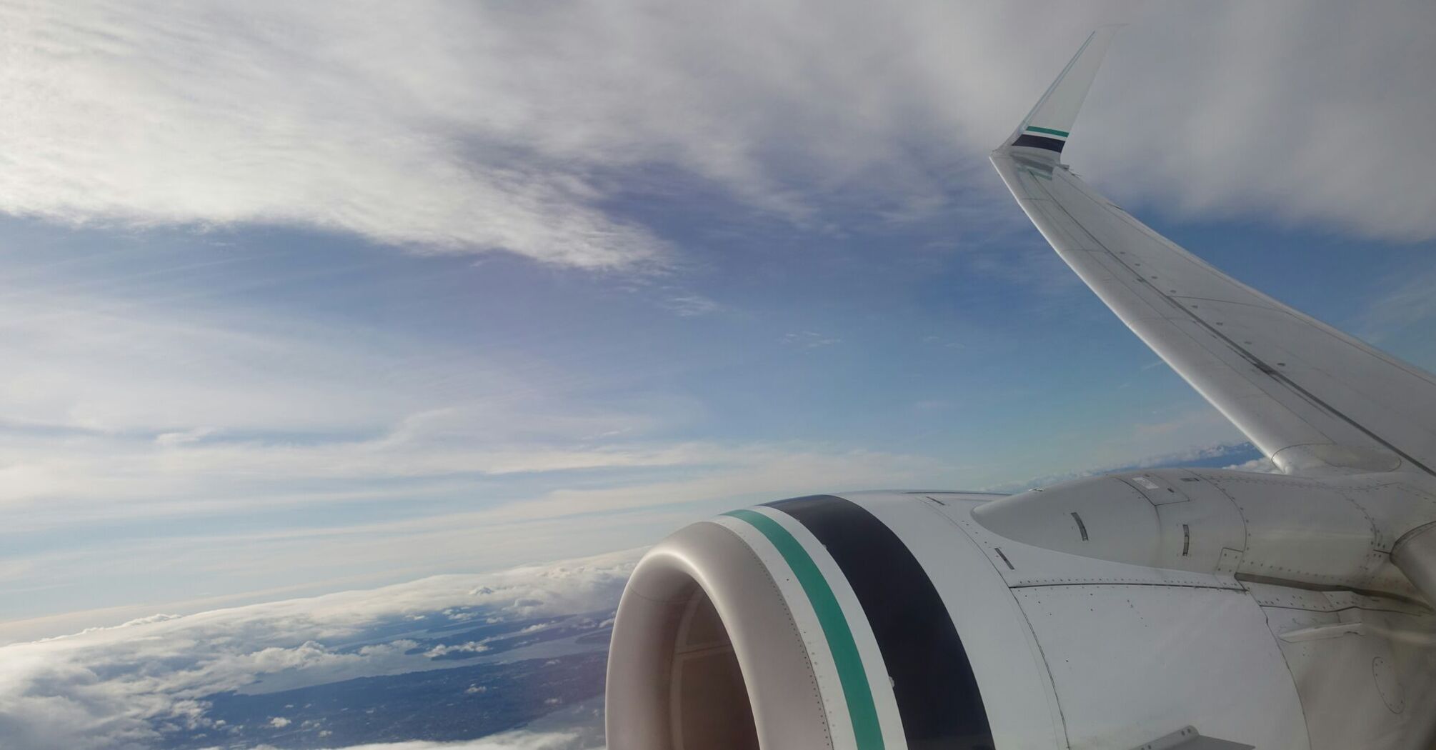 View from an Alaska Airlines plane window showing the wing and engine against a backdrop of clouds and sky