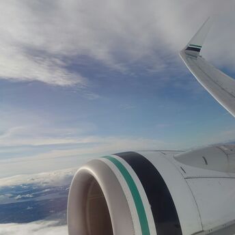View from an Alaska Airlines plane window showing the wing and engine against a backdrop of clouds and sky