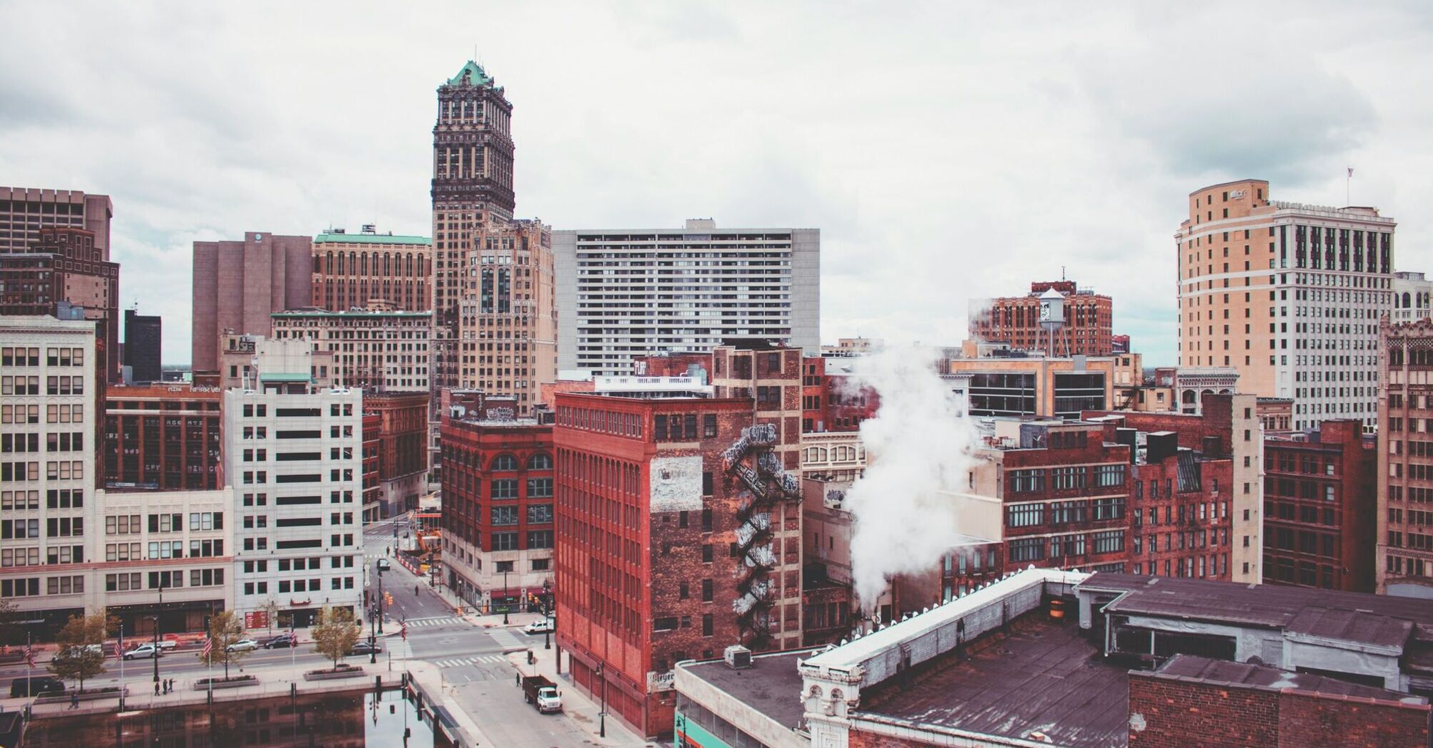 A view of Detroit's downtown with historic and modern buildings, some showing signs of wear, under a cloudy sky