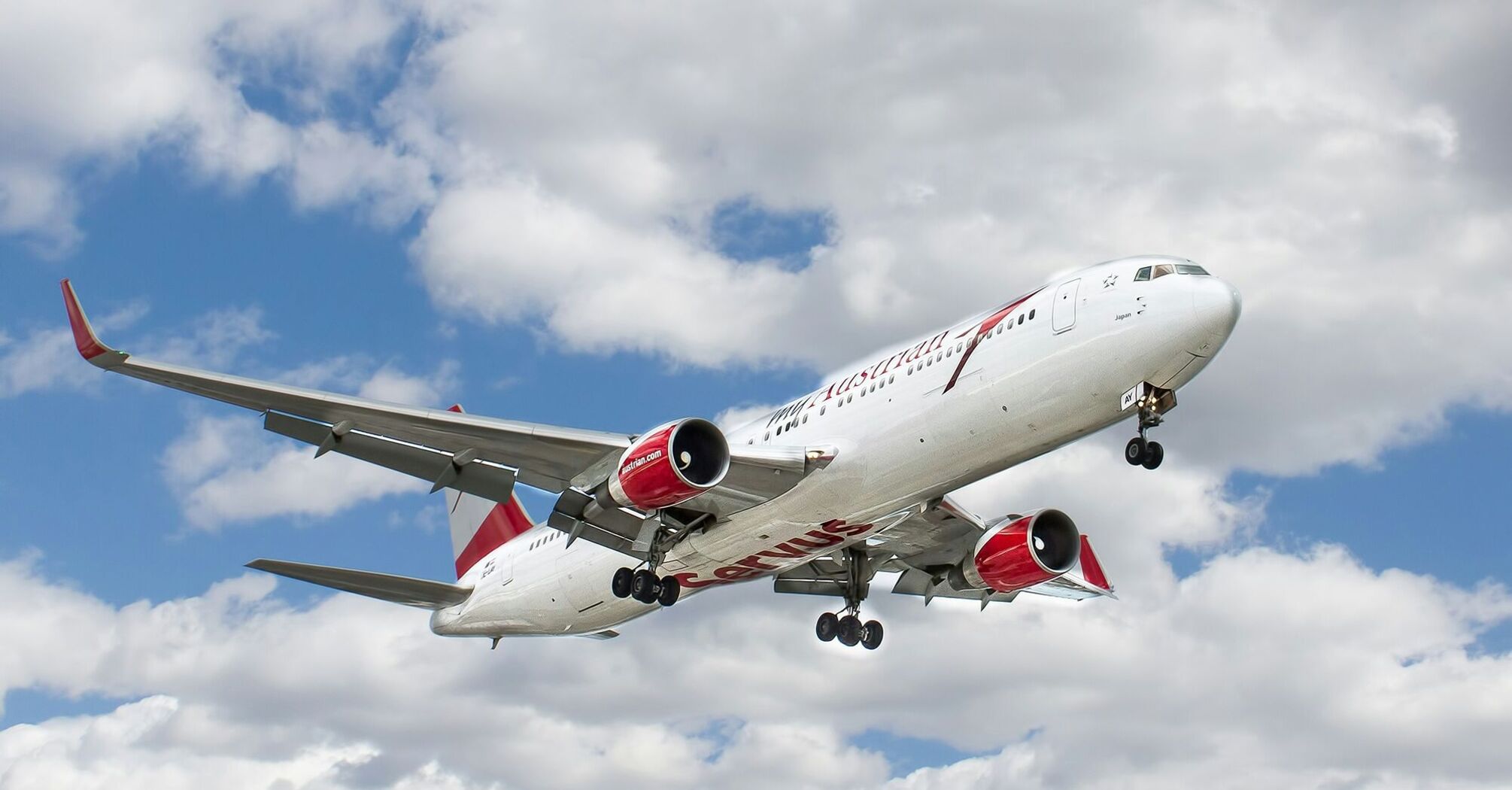 White and red flying airplane under white clouds