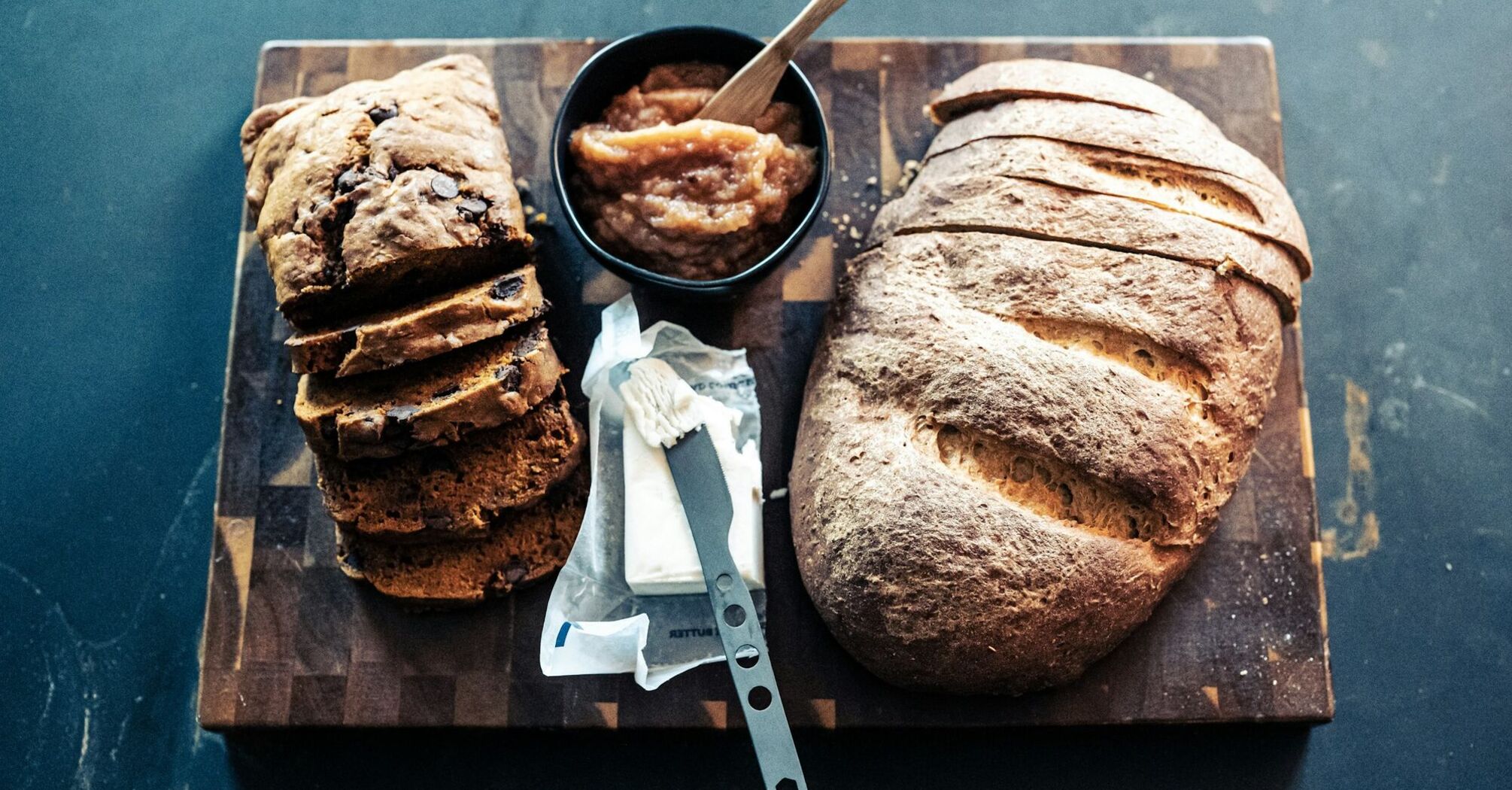 Assorted fresh bread loaves and butter on a wooden boar