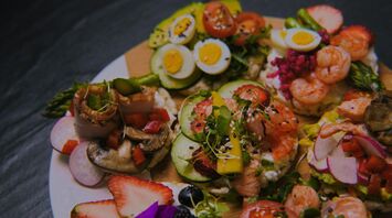 An array of gourmet foods including shrimp, sliced fruits, and salads, artistically arranged on a wooden platter