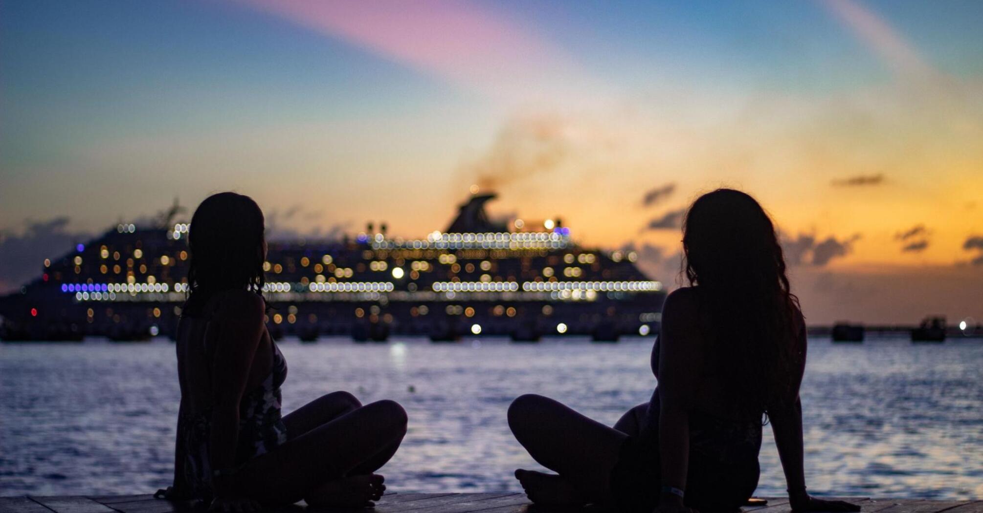 Two girls on the ocean shore against the backdrop of a cruise ship