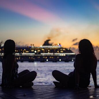 Two girls on the ocean shore against the backdrop of a cruise ship