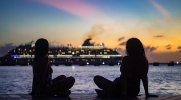 Two girls on the ocean shore against the backdrop of a cruise ship