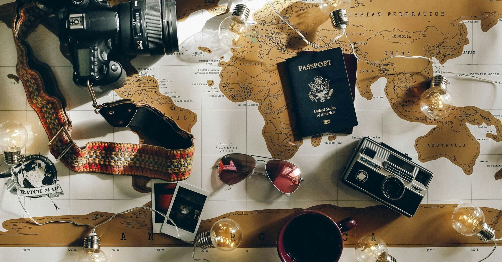 A traveler's flat lay with camera, sunglasses, passport, and world map