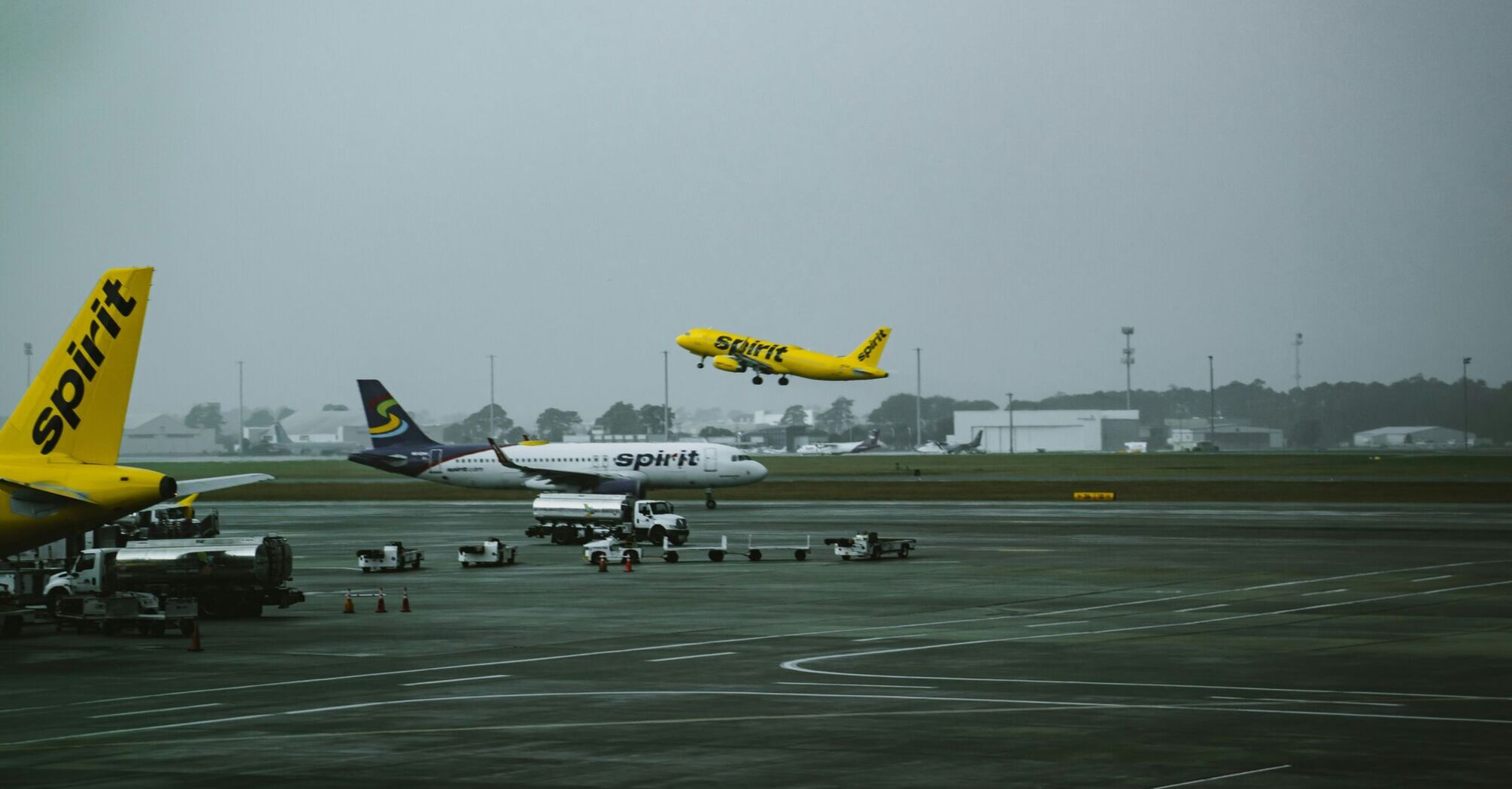 Spirit Airlines aircraft on the tarmac during a gloomy day, with one plane taking off in the background