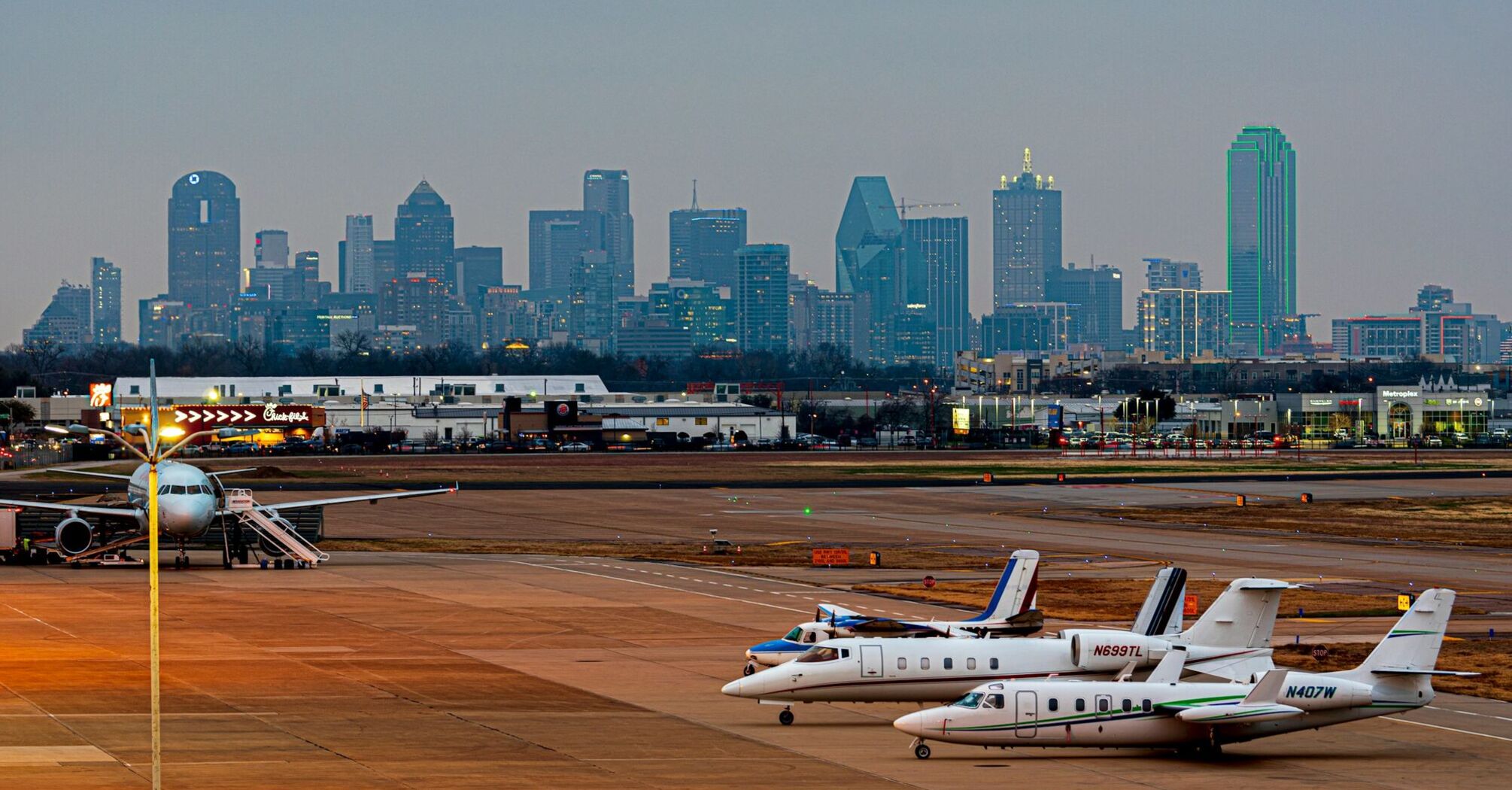 View of Dallas Love Field airport foreground with planes on tarmac and Dallas skyline in background during twilight