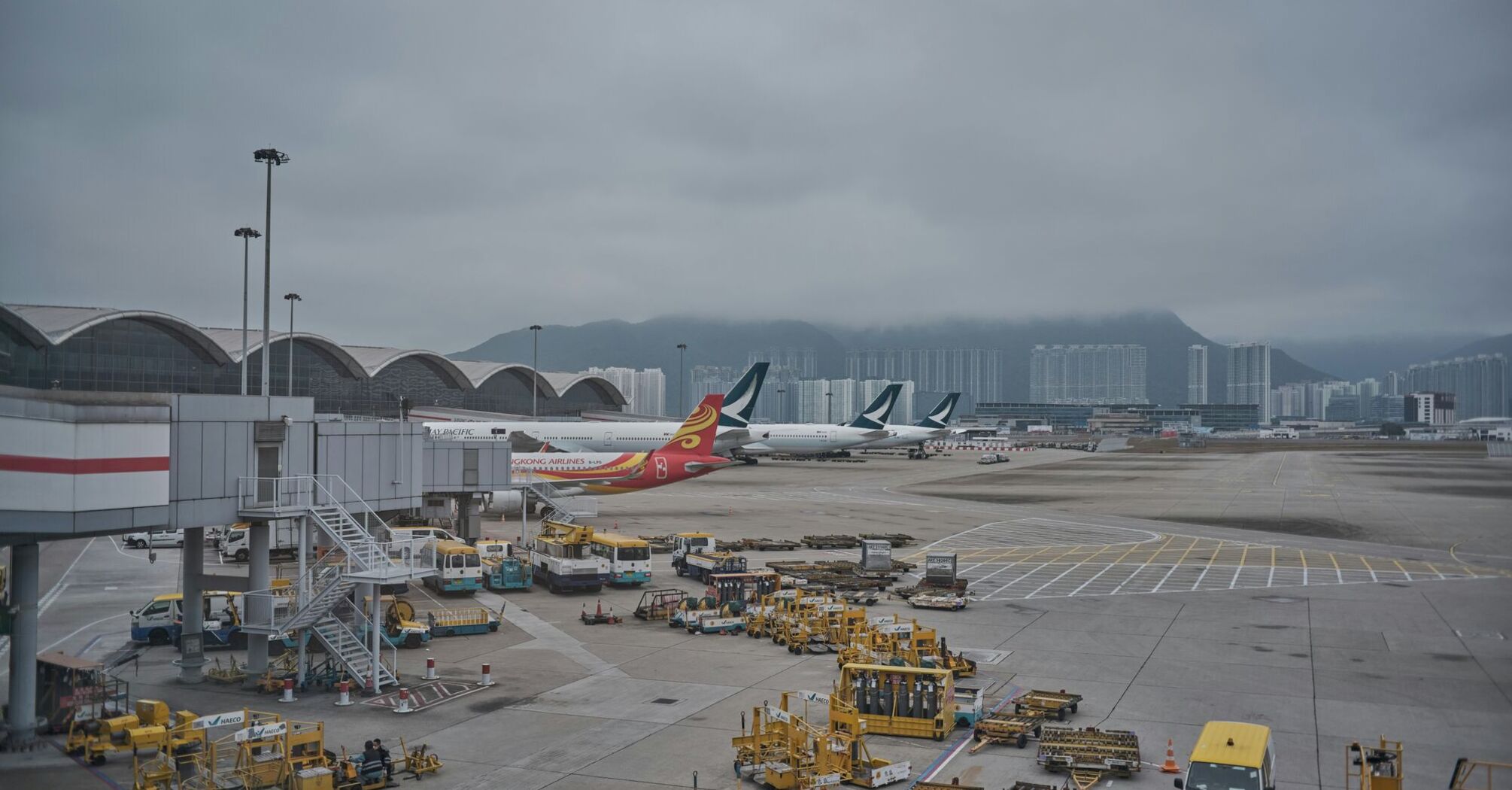 Hong Kong International Airport with active tarmac, aircraft, and cargo vehicles on a cloudy day 