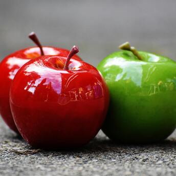 Three glossy apples on a concrete surface, with two red apples and one green apple
