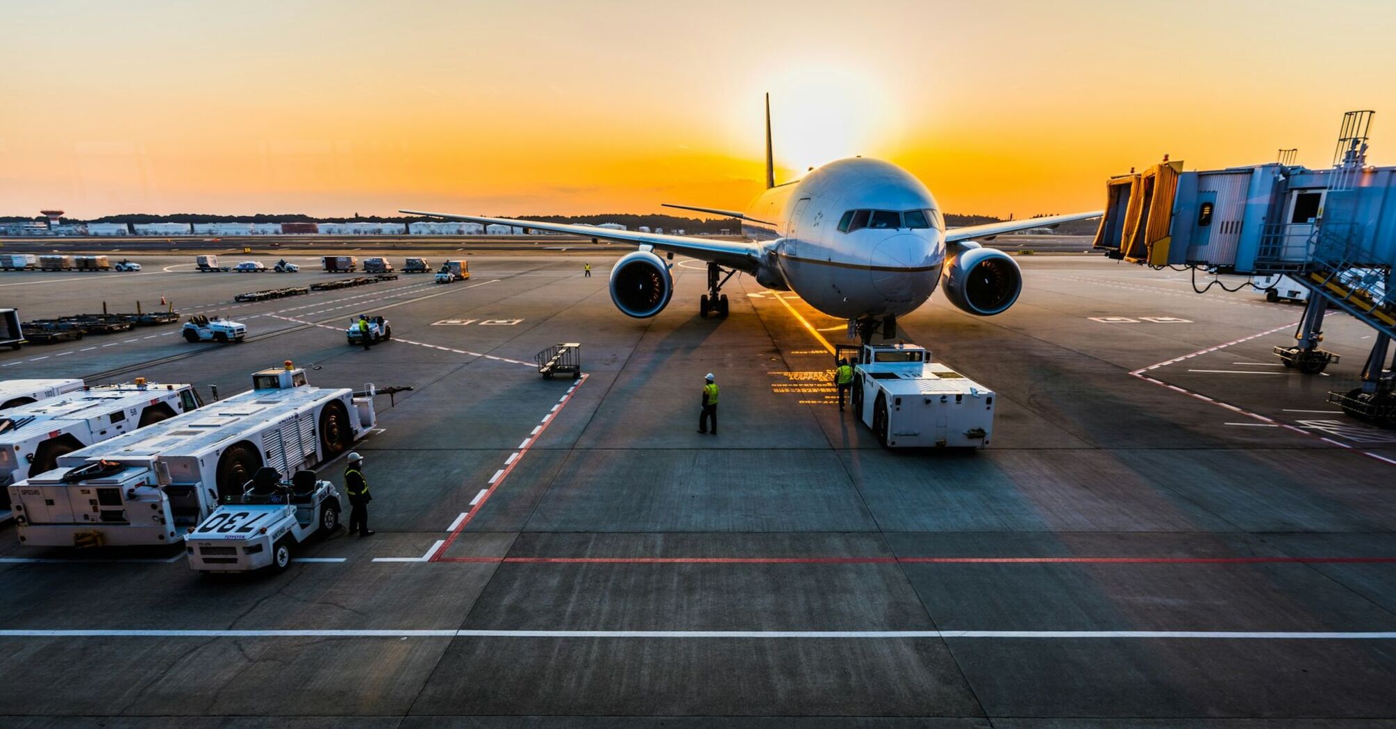 Airplane at airport gate during sunset with ground crew and equipment