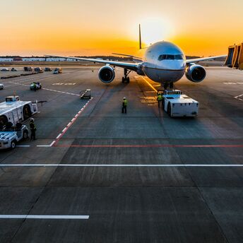 Airplane at airport gate during sunset with ground crew and equipment