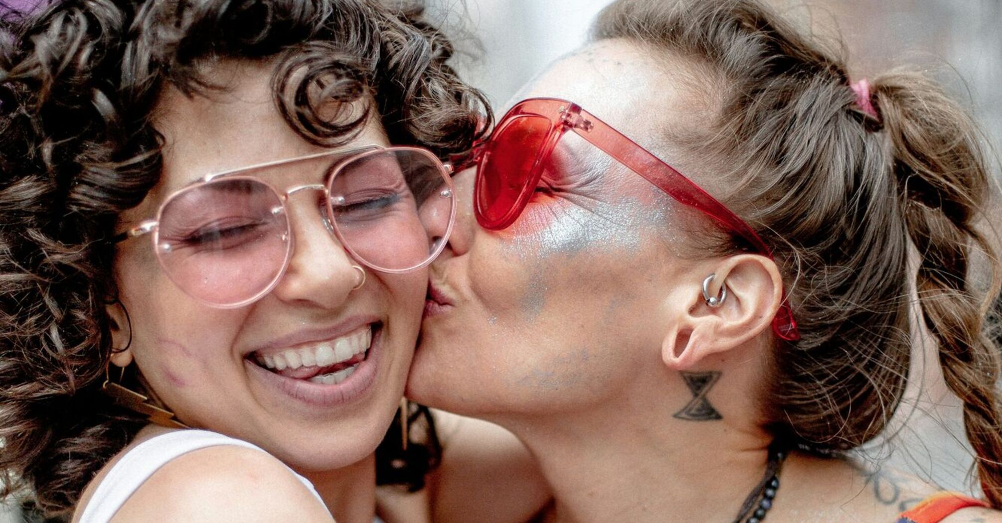 Two women celebrating, sharing a joyful kiss at a Pride