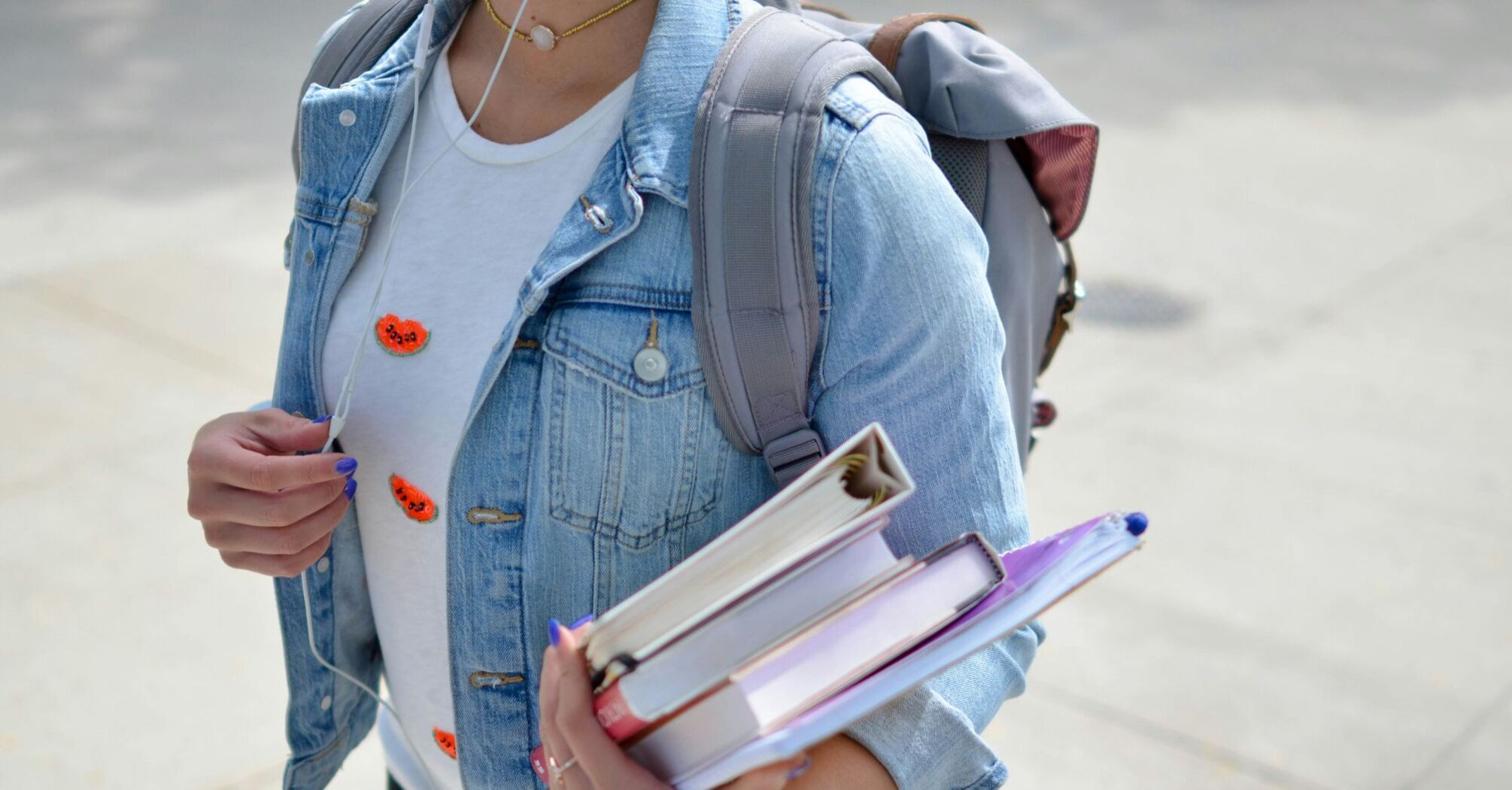 Student with a denim jacket carrying textbooks and a backpack