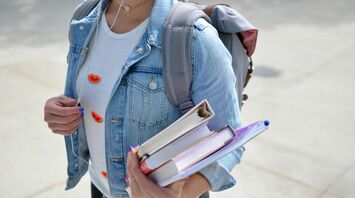 Student with a denim jacket carrying textbooks and a backpack