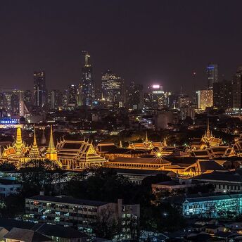 A panoramic night view of Bangkok's cityscape with illuminated Grand Palace and surrounding modern skyscrapers