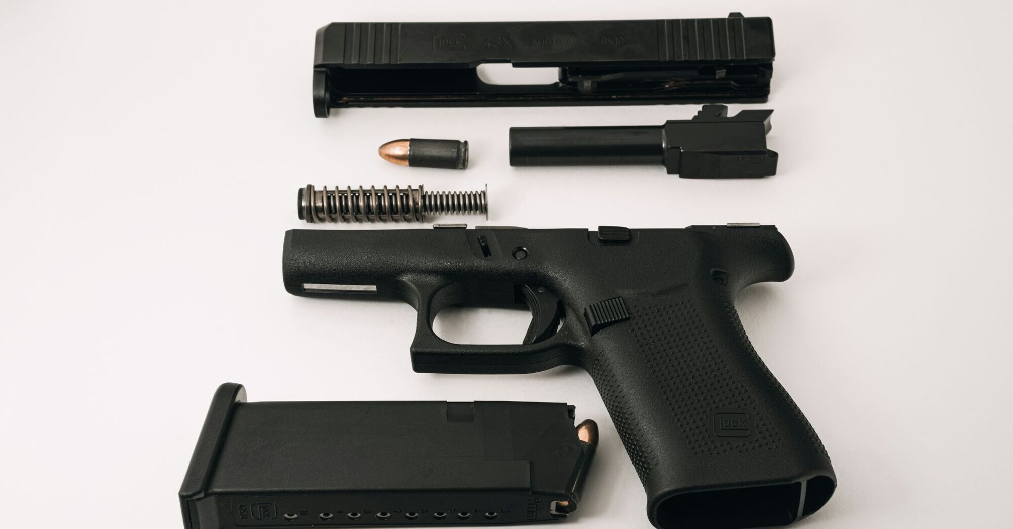 Disassembled black 9mm handgun with parts laid out including the magazine, bullets, slide, and barrel