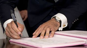 Close-up of a person's hands signing a document on a desk