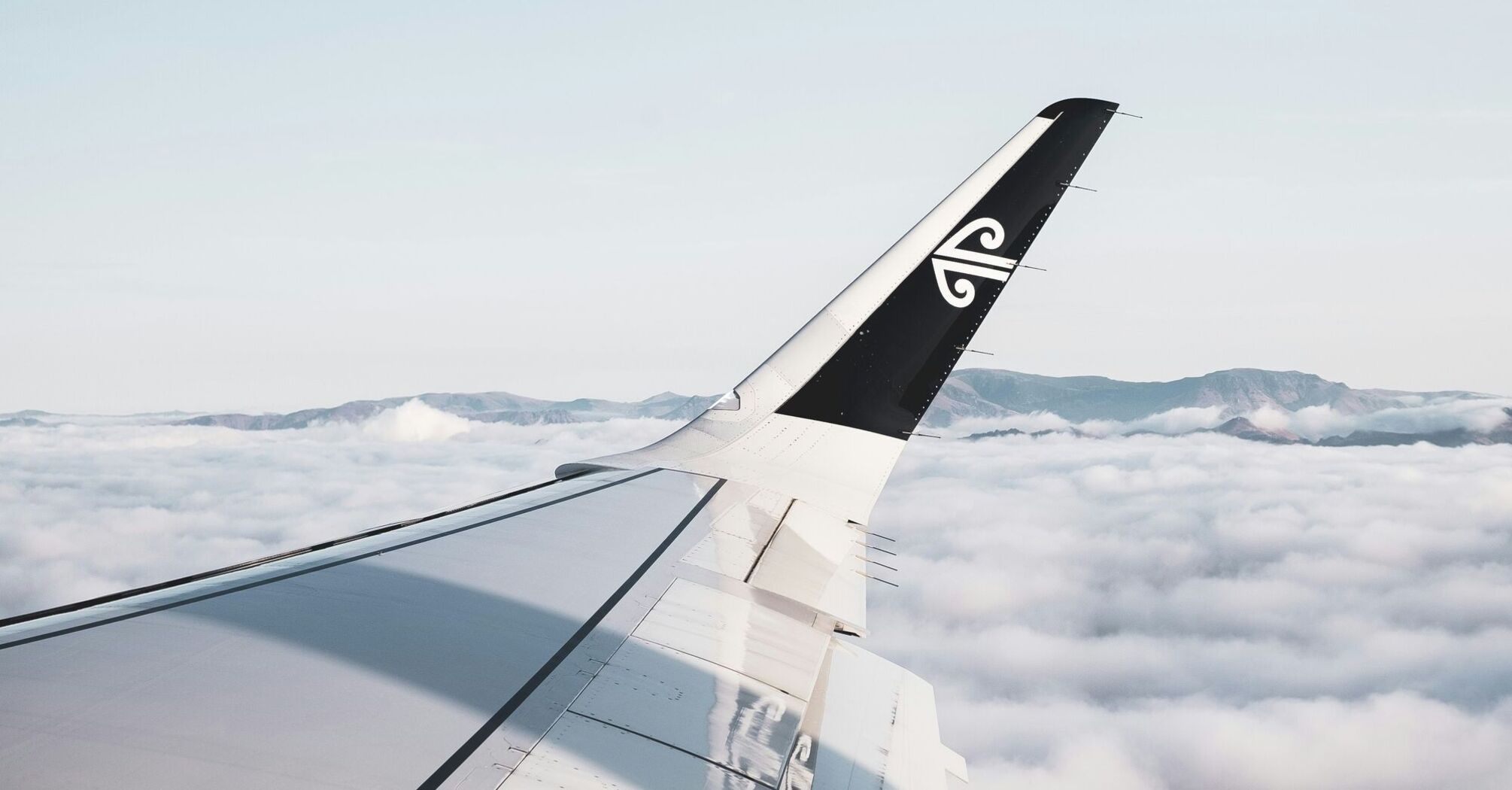 Air New Zealand aircraft wing over clouds with mountains in the distance