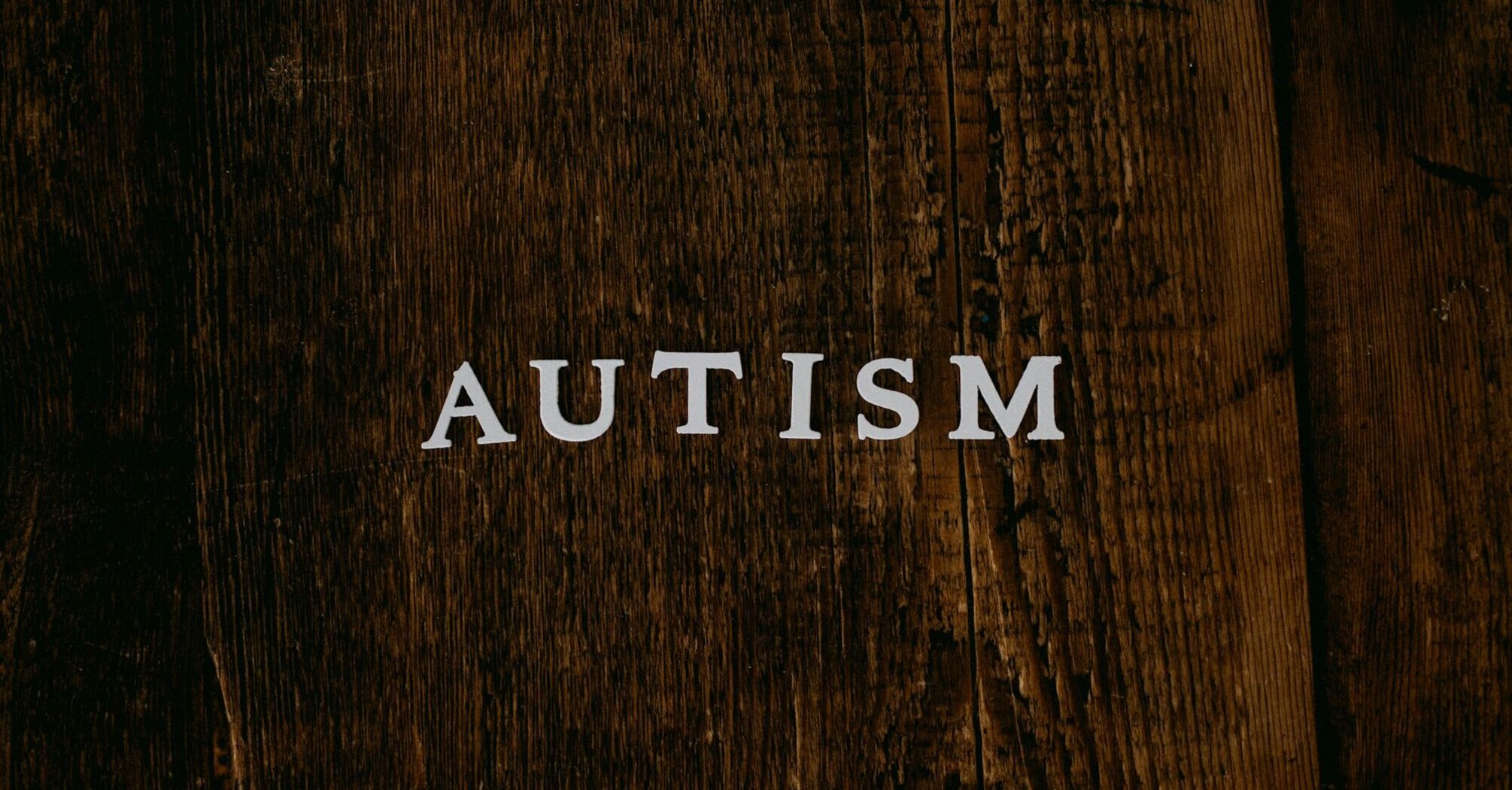 The word 'AUTISM' in white letters on a dark wooden background