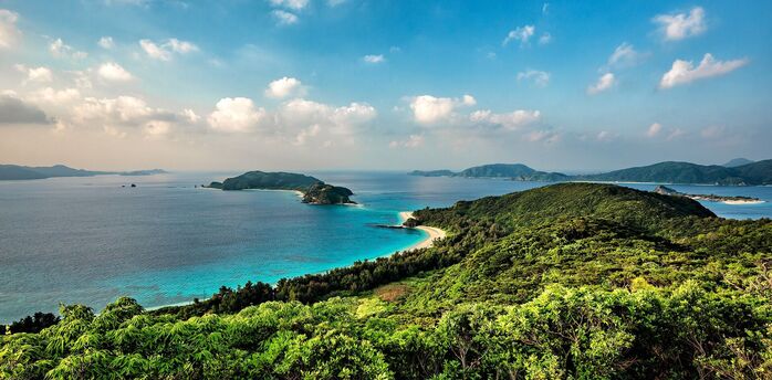 A panoramic view of lush green hills overlooking the crystal-clear blue waters surrounding the islands of Okinawa, Japan