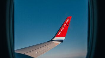 View from an airplane window showing a wing with the Norwegian Air logo against a clear blue sky