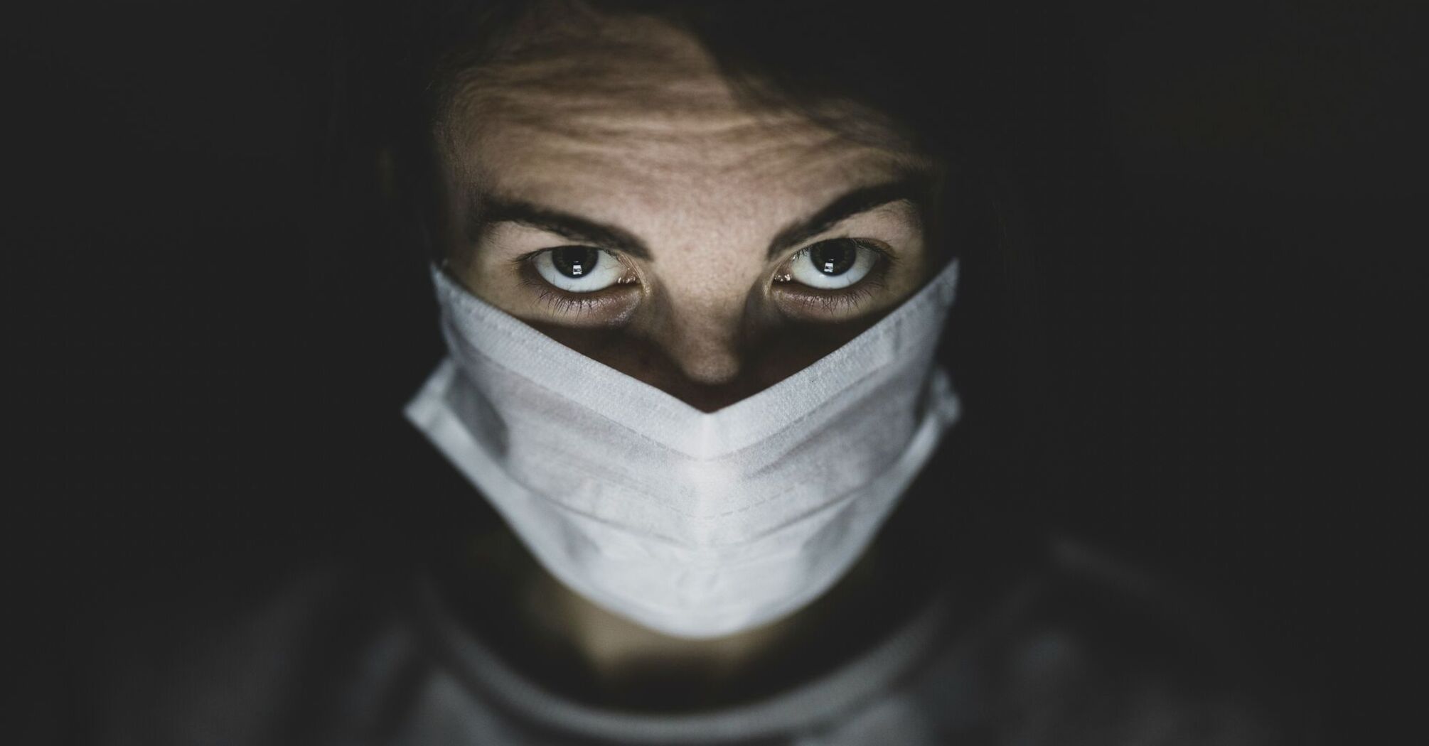 Person with intense gaze wearing a surgical mask in dim lighting