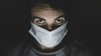 Person with intense gaze wearing a surgical mask in dim lighting