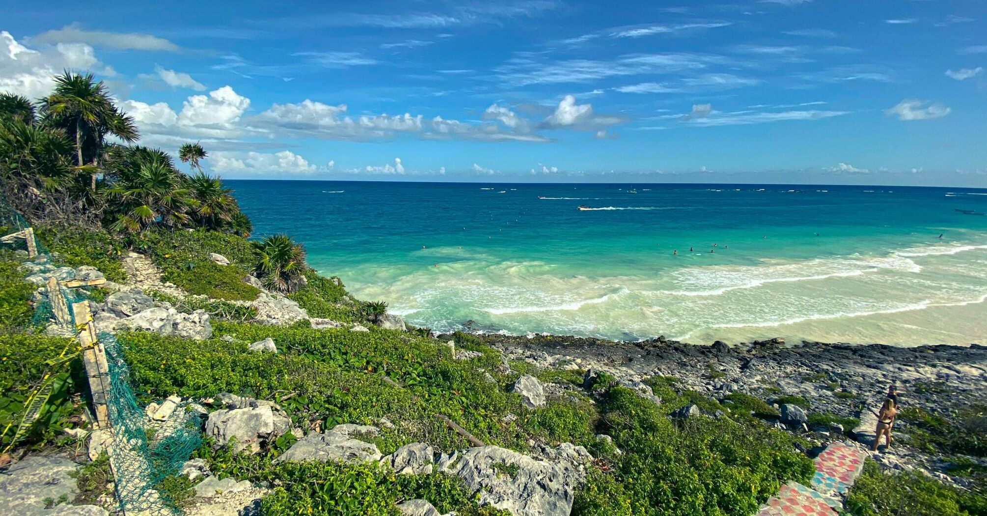Vibrant view of the turquoise Caribbean Sea from a rocky coastline with lush greenery and a clear blue sky in Quintana Roo