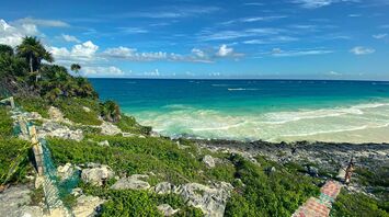 Vibrant view of the turquoise Caribbean Sea from a rocky coastline with lush greenery and a clear blue sky in Quintana Roo