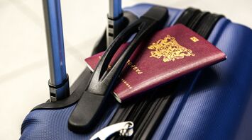 A blue suitcase with a British passport and sunglasses on top