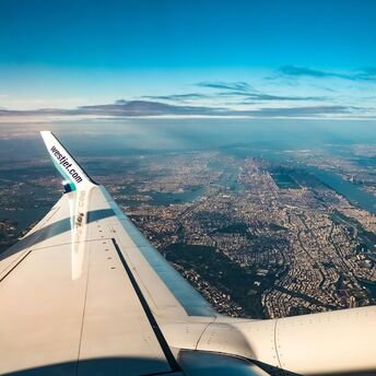 An airplane wing with a WestJet logo flying over a sprawling cityscape