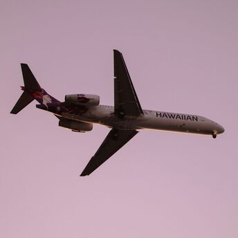 A Hawaiian Airlines aircraft in flight against a pink sky backdrop