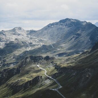 A winding road stretches across the rugged and mountainous landscape of the Austrian Alps