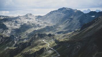 A winding road stretches across the rugged and mountainous landscape of the Austrian Alps