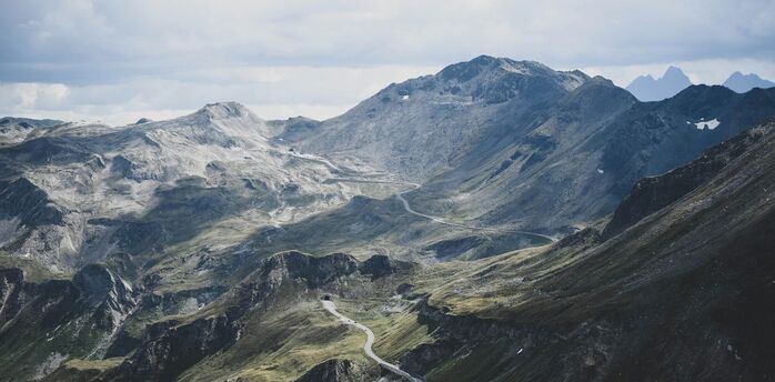 A winding road stretches across the rugged and mountainous landscape of the Austrian Alps