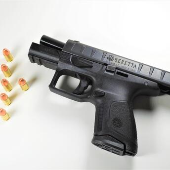 Handgun with a black finish, displayed on a white background, alongside eight copper-tipped bullets arranged in a line
