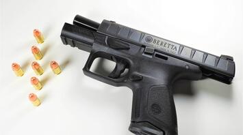 Handgun with a black finish, displayed on a white background, alongside eight copper-tipped bullets arranged in a line