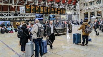 People with luggage waiting in an airport or train station terminal, checking information on electronic display boards