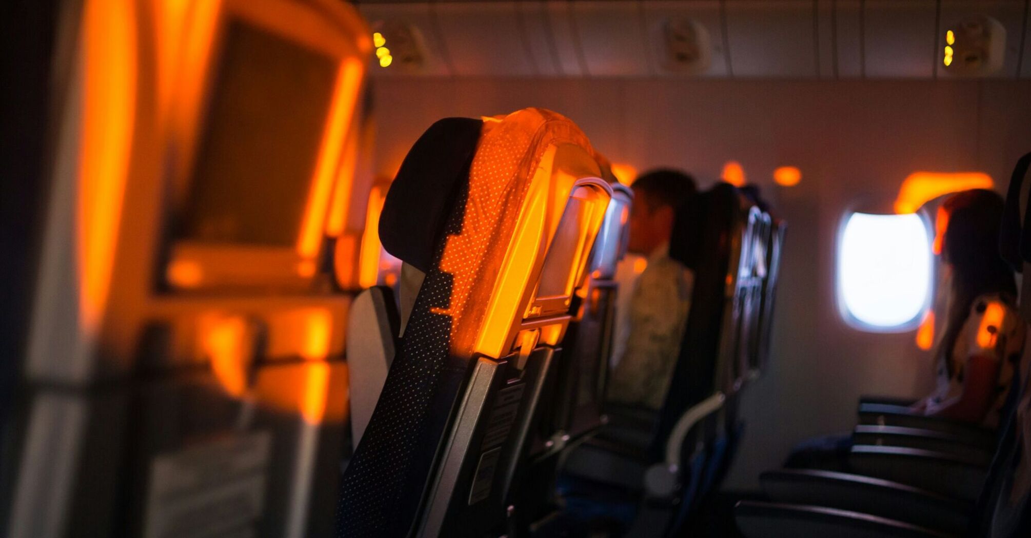 An airplane cabin with dimmed lighting, showing rows of seats and a window in the background