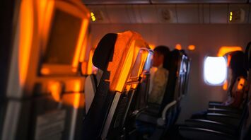 An airplane cabin with dimmed lighting, showing rows of seats and a window in the background