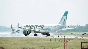 Frontier Airlines plane taxiing on an airport runway with a polar bear design on its tail fin