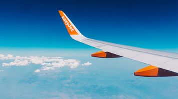 An airplane wing with the easyJet logo flying over a landscape with clouds and blue sky