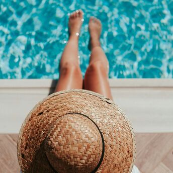 Person relaxing by the pool, wearing a straw hat