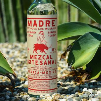 A bottle of mezcal riessanal sitting on a bed of gravel