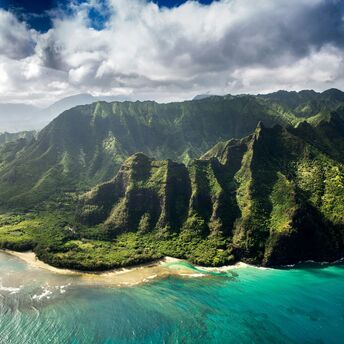 Aerial view of a lush, mountainous coastline in Hawaiʻi with clear blue waters