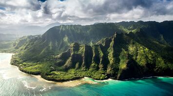 Aerial view of a lush, mountainous coastline in Hawaiʻi with clear blue waters