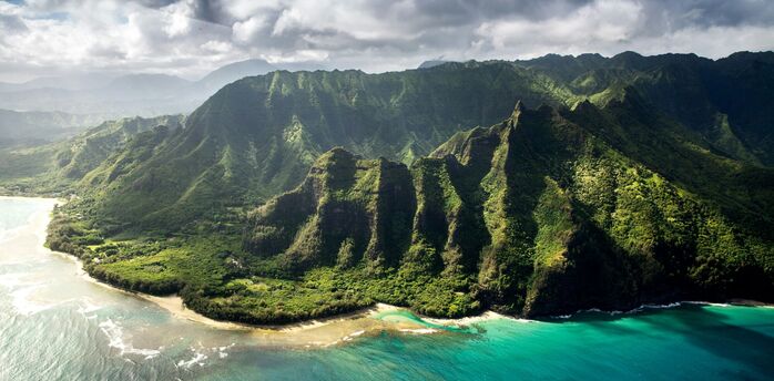 Aerial view of a lush, mountainous coastline in Hawaiʻi with clear blue waters